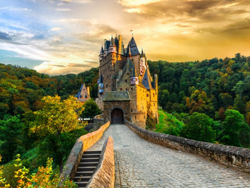 Burg Eltz met hoge torens, erkers en vakwerkversieringen, midden in het bos bij bewolkte hemel.