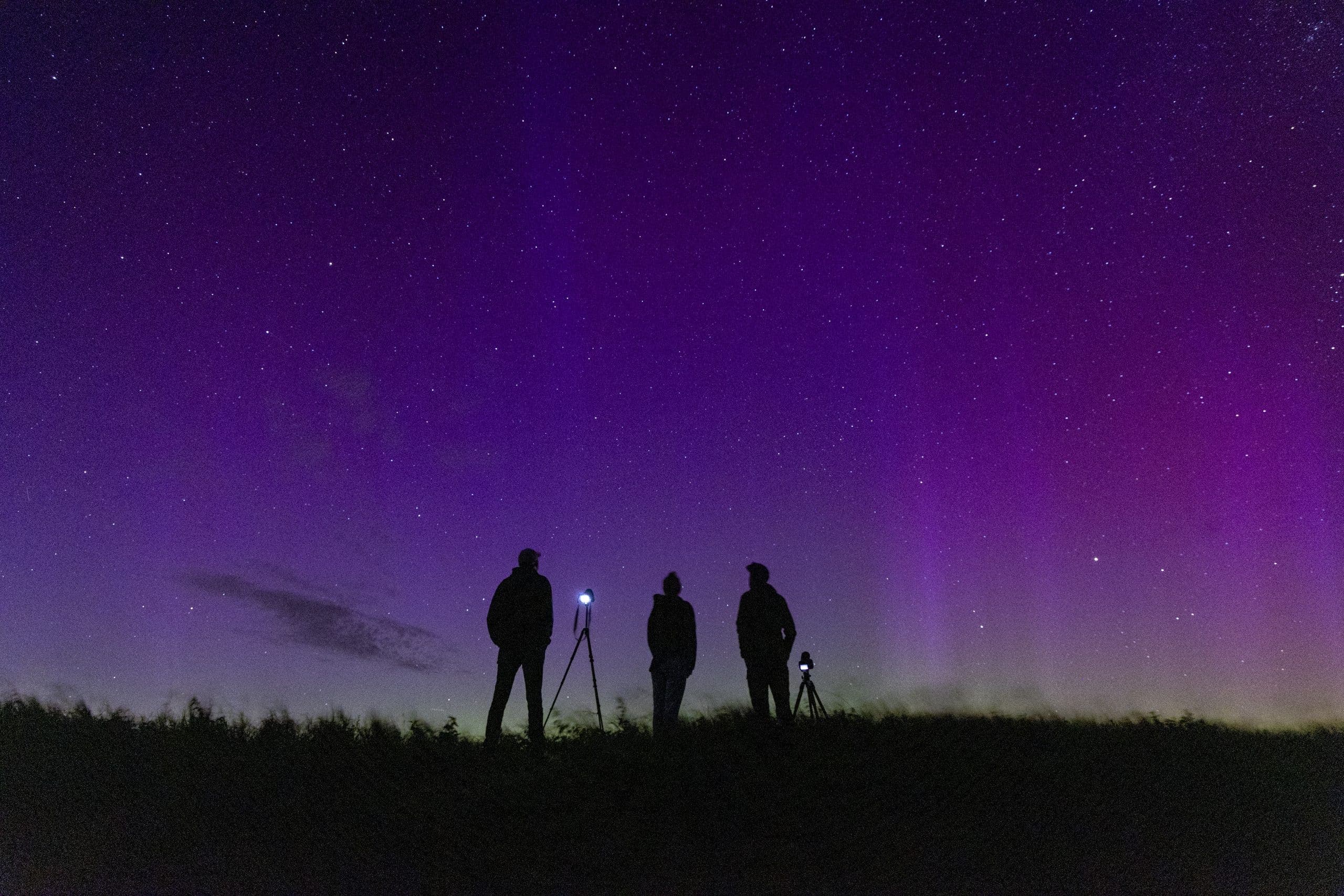 Drie mensen met het noorderlicht op de achtergrond