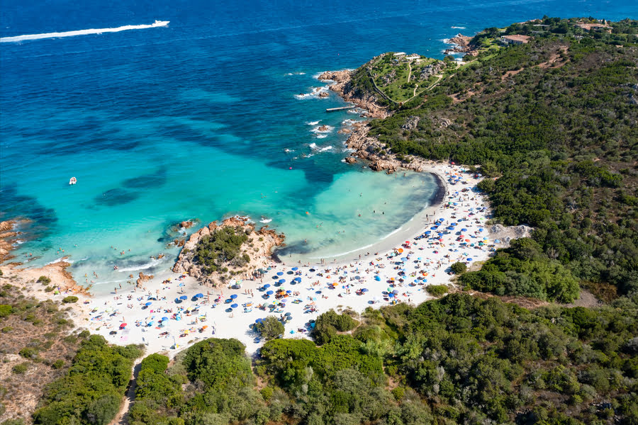 luchtfoto van een klein, parelwit strand, een bos en helderblauw water