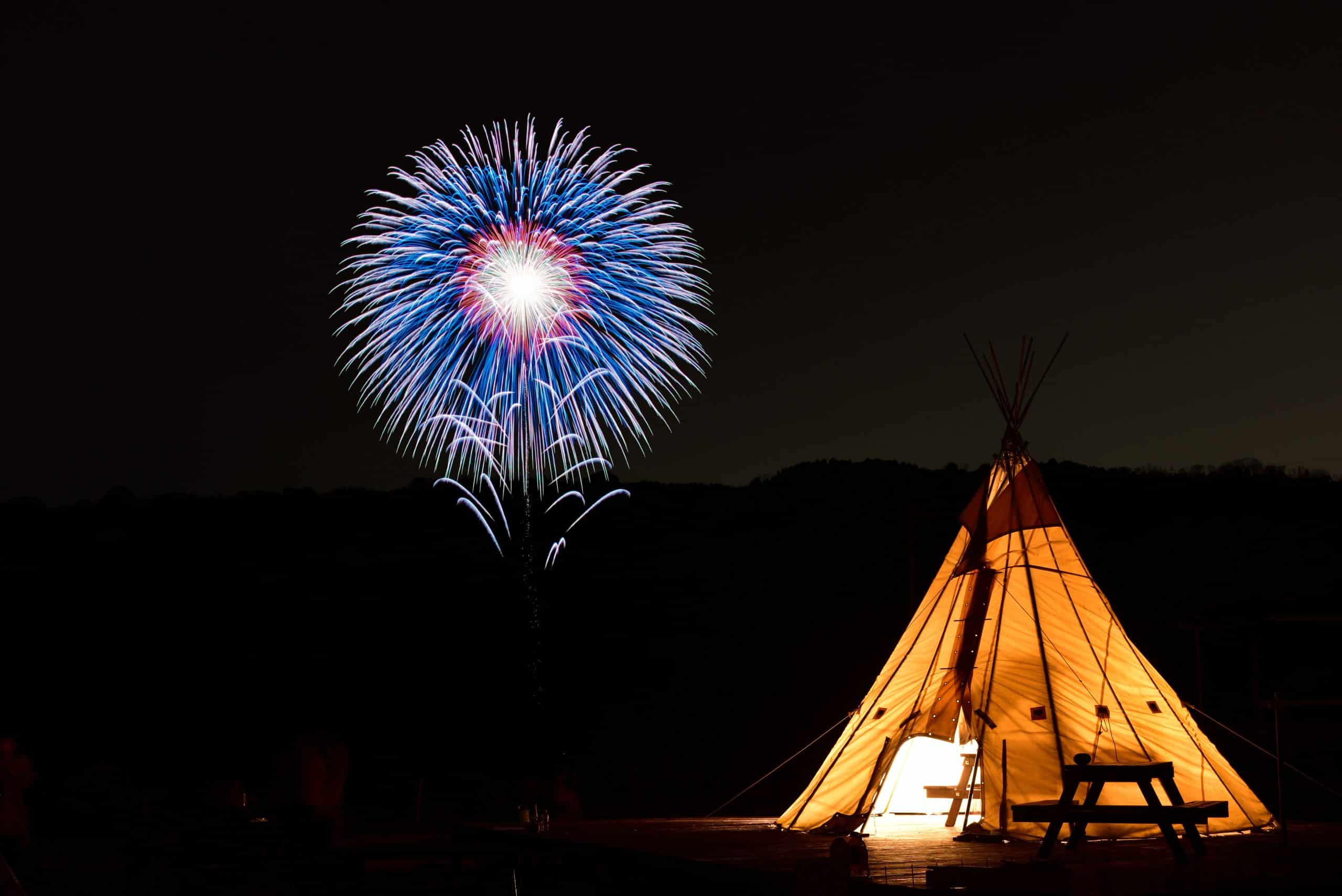 Verlichte tent in het donker met vuurwerk op de achtergrond